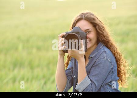 Bonne femme qui prend des photos avec un appareil photo reflex numérique qui vous regarde dans un champ de blé Banque D'Images