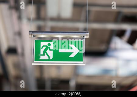 Essen, Allemagne - 26 mars 2022 : panneau lumineux de sortie de secours suspendu au plafond. Avec la figure courante et une flèche pointant vers la droite. Banque D'Images