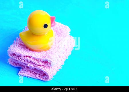 Bébé canard en caoutchouc placé sur une pile de serviettes de bain miniatures isolées sur fond bleu. Concept de bain amusant. Banque D'Images