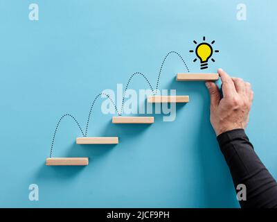 Main mâle arrange une échelle en bois avec le symbole d'ampoule IDEA. Échelle de succès, brainstorming, atteindre une idée ou un concept de génération d'idée Banque D'Images