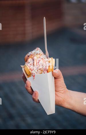 Main tenant une gaufre à bulles avec de la crème glacée, de la sauce aux fraises et des flocons de noix de coco Banque D'Images