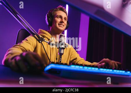 Joyeux joueur professionnel en streaming esport Tournoi avec microphone et casque, en profitant d'un jeu multijoueur. Joueur de compétition jouant à des jeux vidéo en ligne à la maison. Couleur néon. Concept de cybersport Banque D'Images