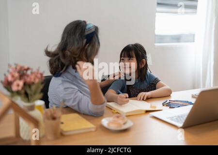 Grand-mère de femme plus âgée et petite petite-fille grand-enfant avec devoirs étude à distance. Une vieille femme attentionnée et mûre donne une leçon privée à un petit élève Banque D'Images