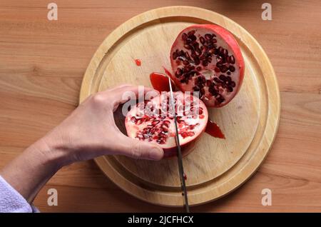 Couper et ouvrir un fruit grenade rouge (Punica granatum) avec un couteau sur une planche en bois Banque D'Images