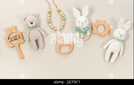 Arrière-plan des jouets pour bébés. Lapin tricoté, ours en peluche fait main et anneaux de dentition en bois pour bannière sur une bannière beige pastel. Hochets et jouets en bois pour un joli b Banque D'Images