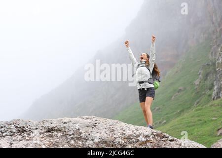 Un trekker excités qui élève les bras célébrant le succès dans la montagne un jour brumeux Banque D'Images