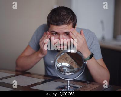 guy vérifiant sa peau. Le jeune homme regardant dans le miroir touche le visage avec le bouton se sent mécontent. Traitement anti-acné de soin de la peau, déséquilibre hormonal, stress, régime alimentaire, problème de peau, concept d'aspect de rétrodiffusion Banque D'Images