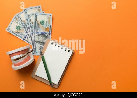 Composition de pose à plat avec modèle de typographie dentaire pédagogique et argent avec carnet sur table colorée, vue de dessus. Traitement coûteux. Banque D'Images