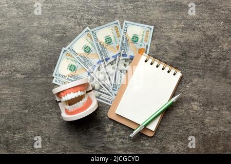 Composition de pose à plat avec modèle de typographie dentaire pédagogique et argent avec carnet sur table colorée, vue de dessus. Traitement coûteux. Banque D'Images