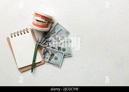 Composition de pose à plat avec modèle de typographie dentaire pédagogique et argent avec carnet sur table colorée, vue de dessus. Traitement coûteux. Banque D'Images