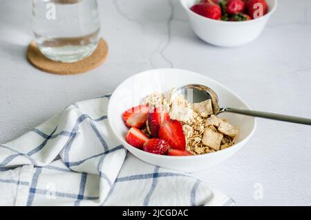 Granola. Granola maison avec fraise fraîche pour le petit déjeuner dans une assiette blanche sur fond de béton gris. Banque D'Images