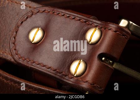 Partie d'une ceinture en cuir marron avec boucle en métal sur fond noir. Banque D'Images