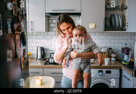 Maman nourrit un petit enfant à la maison avec du yaourt à la cuillère. Concept de famille Banque D'Images