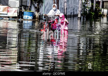 Sidoarjo, Indonésie. 13th juin 2022. Une mère et sa fille poussent leurs vélos dans les eaux d'inondation après une forte pluie à Waru à Sidoarjo, Java-est, Indonésie, 13 juin 2022. Credit: Kurniawan/Xinhua/Alay Live News Banque D'Images