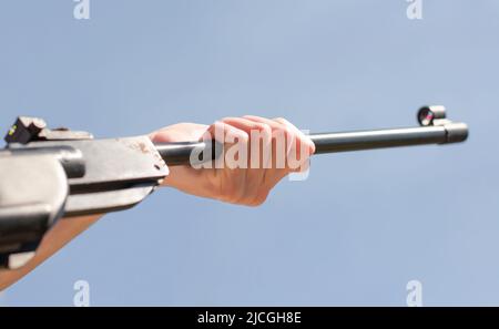 Une main tient le canon d'une carabine à air comprimé contre un ciel bleu Banque D'Images