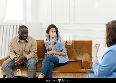 Divers couple parlant à la femme psychologue des problèmes de relation. Thérapie conjugale. Réconciliation familiale. Banque D'Images