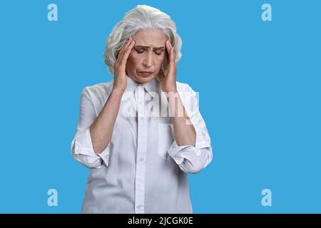 Femme âgée surtraitée souffrant de maux de tête sur fond bleu. Concept de problème de santé. Banque D'Images