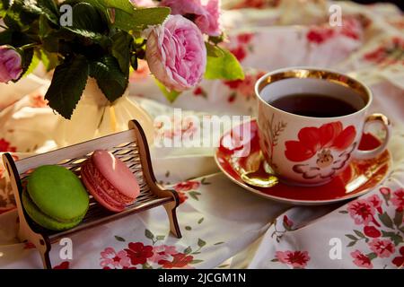 Macarons français sur le banc en bois miniature dans le style d'un café. Décorations de rose de thé et tasse de thé. Temps de thé. Photographie esthétique de style de vie. Banque D'Images