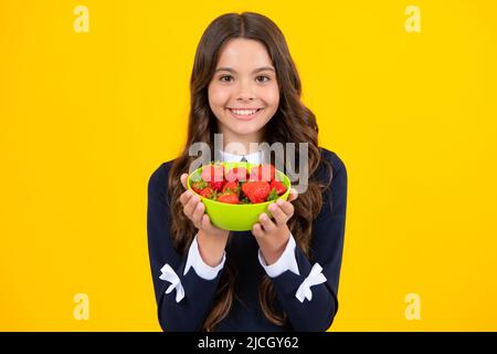 Un enfant de l'adolescence tient un bol à fraises sur fond jaune. Banque D'Images