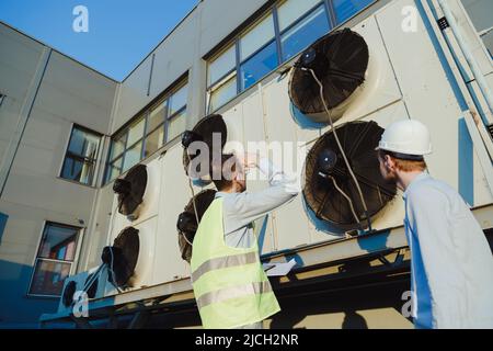 Réunion d'architecte et de superviseur sur le chantier de construction. Discussion sur le plan. Deux ouvriers de la construction travaillent ensemble au service d'entretien des réfrigérateurs hvac Banque D'Images