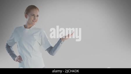 Une travailleuse de santé caucasienne tient un objet invisible contre l'espace de copie sur fond gris Banque D'Images