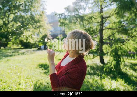 Une femme souffle sur une pissenlit lors d'une journée d'été ensoleillée. Banque D'Images