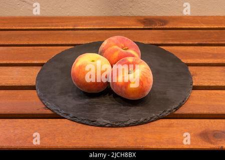 Assiette avec trois pêches mûres rougeâtres sur une table en bois Banque D'Images