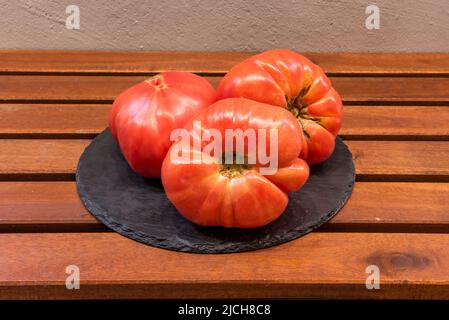 Assiette de trois tomates roses épaisses, mûres et prêtes à manger sur une table en bois Banque D'Images