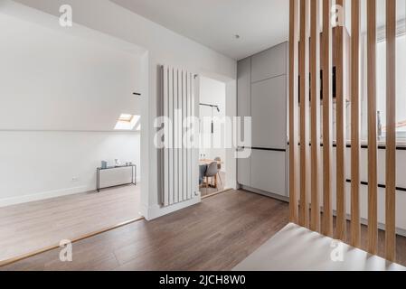 Avant d'une cuisine avec mobilier en bois blanc combiné à des meubles en bois, un long radiateur en aluminium et l'accès à un salon avec un c incliné Banque D'Images