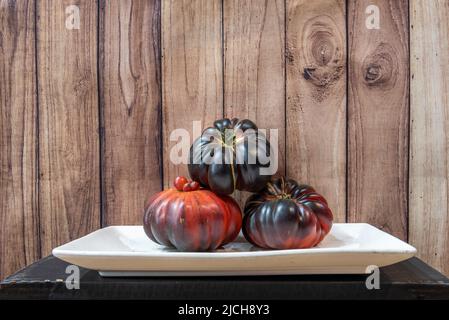 plateau blanc avec trois tomates bleues mûres et fond en bois foncé Banque D'Images