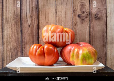 plateau blanc avec trois grandes tomates roses mûres et fond en bois foncé Banque D'Images