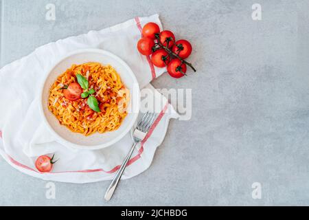 Assiette avec vue sur le dessus de pâtes fraîches maison cuites avec sauce crémeuse à la tomate, fruits de mer et parmesan, décorée de feuilles de basilic sur le gris Banque D'Images