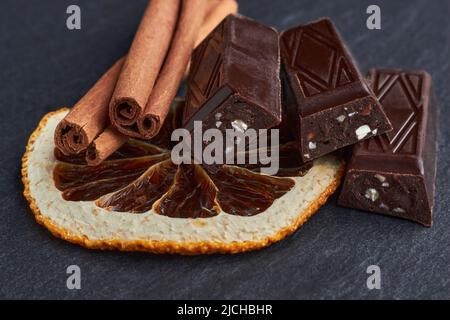 Barres de chocolat noir avec amandes hachées, quartiers d'orange séchés et bâtonnets de cannelle. Gros plan. Journée chocolat noir Banque D'Images