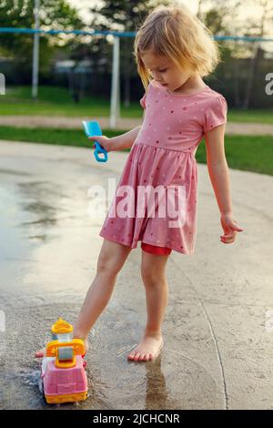 Un petit enfant joue au coussin d'eau avec de l'eau et des jouets d'extérieur. Petite fille s'amuser à l'aire de jeux avec des fontaines en été. Banque D'Images