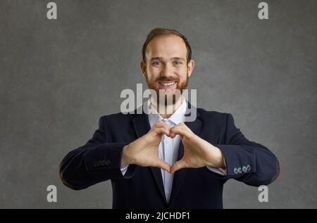 Homme d'affaires d'âge moyen en costume souriant montrant la forme du cœur comme symbole de l'amour. Banque D'Images