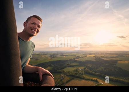Homme profitant de la vue depuis un ballon d'air chaud pendant le vol sur un paysage magnifique au coucher du soleil. Thèmes aventure, liberté et voyage. Banque D'Images