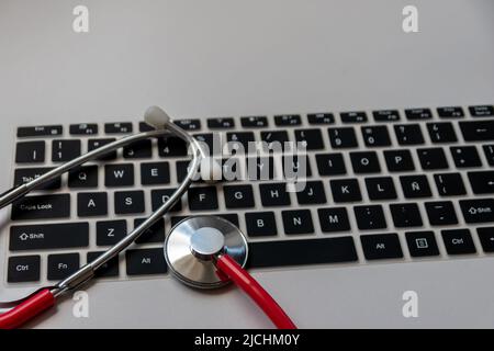 Stéthoscope rouge sur clavier d'ordinateur noir sur le bureau blanc montre le bureau numérique des médecins avec des dossiers numériques des patients pour le diagnostic médical et cardiolog Banque D'Images