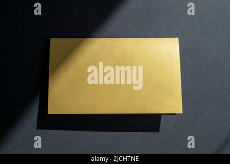 Maquette de carte de visite dorée, invitation sur surface noire avec ombres et lumière du soleil Banque D'Images