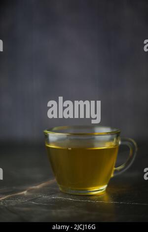 Thé vert infusé éclairé dans une tasse transparente sur fond sombre Banque D'Images