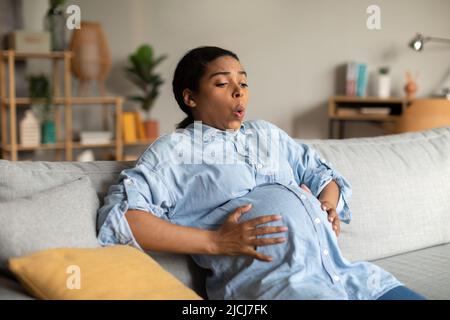 Femme noire enceinte ayant un spasme touchant la respiration de ventre à la maison Banque D'Images