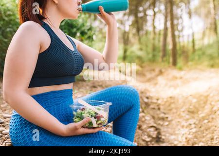 plan court de jeune sportswoman assis boire et manger sainement après l'entraînement sportif. fille jouant au sport à l'extérieur. santé et bien-être Banque D'Images