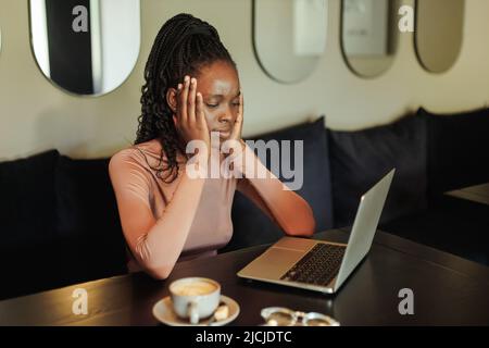 Une course mixte inquiète et fâchée femme d'affaires afro-américaine, surtravaillant en ligne avec un ordinateur portable dans un bureau créatif. Maux de tête Banque D'Images