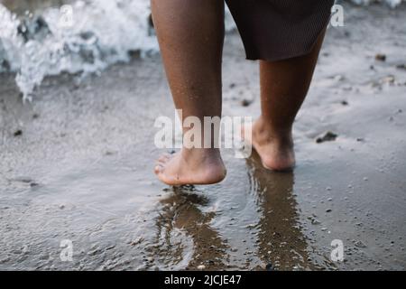 Courte peau foncée pieds nus femme jambes marchant à travers la côte de mer, plage, mousse de lavage. Personne multiculturelle, vacances d'été Banque D'Images