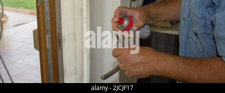 Image des mains d'un handyman qui, après avoir démonté une poignée d'une fenêtre française, effectue des travaux d'entretien en la lubrifiante. Bannière Banque D'Images