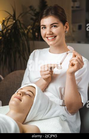 Portrait d'une jeune esthéticienne avec un dispositif pour les procédures cosmétiques, regardant la caméra et souriant assis près du patient. Soins de la peau. Médical Banque D'Images