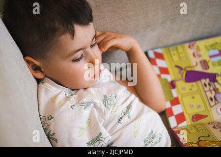 Garçon lisant le livre d'images dans l'après-midi à la maison, allongé sur le canapé. Concept de famille, d'enfance, de paternité, de loisirs et de personnes. Banque D'Images