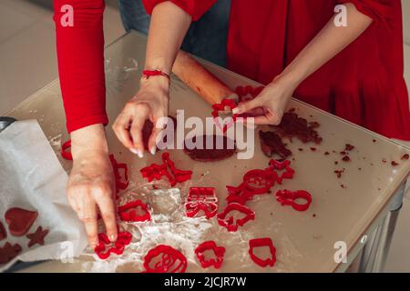 Pâtisserie de Noël, mains d'homme et de femme tenant emporte-pièce, couleur rouge. Maison cuisine confortable, bonne Saint-Sylvestre, moments de la veille de Noël. Banque D'Images