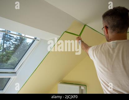 Le peintre enlève le ruban de masquage et crée une bordure nette entre une partie peinte en jaune et en blanc d'un mur. Banque D'Images