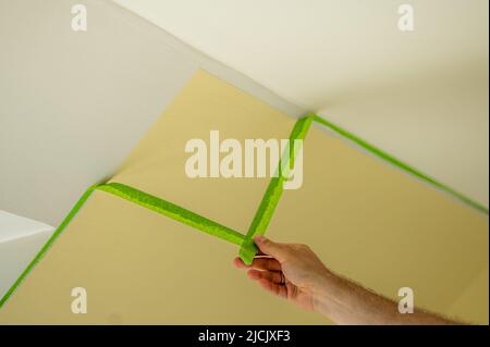 Le peintre enlève le ruban de masquage et crée une bordure nette entre une partie peinte en jaune et en blanc d'un mur. Banque D'Images