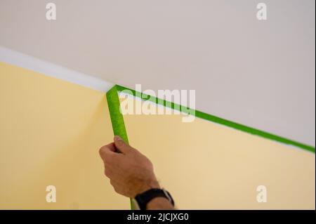 Le peintre enlève le ruban de masquage et crée une bordure nette entre une partie peinte en jaune et en blanc d'un mur. Banque D'Images